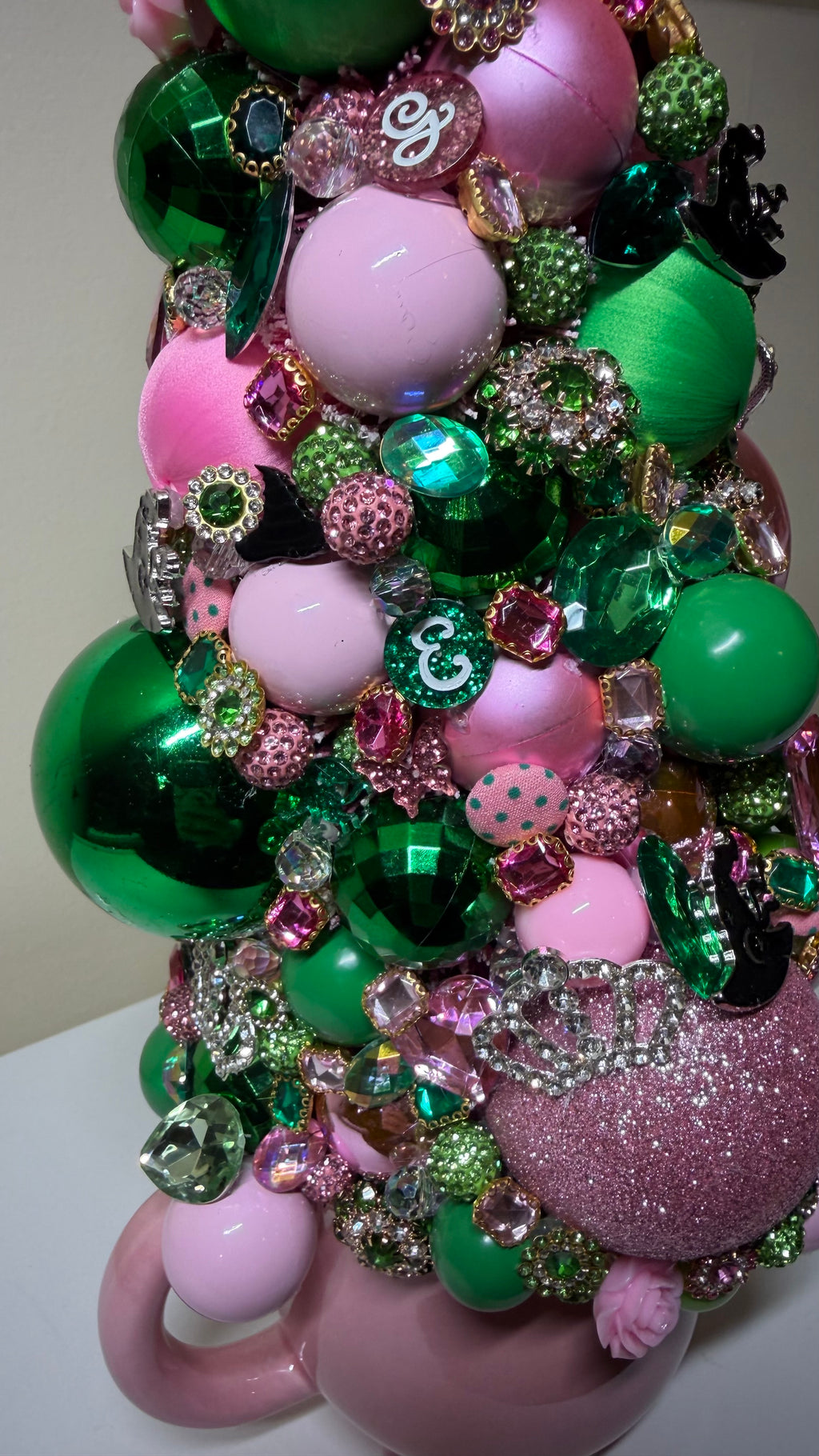 A unique and decorative Christmas or Table Top tree made from pink and green ornaments, beads, and sequins, displayed on a white mantelpiece next to a round mirror.