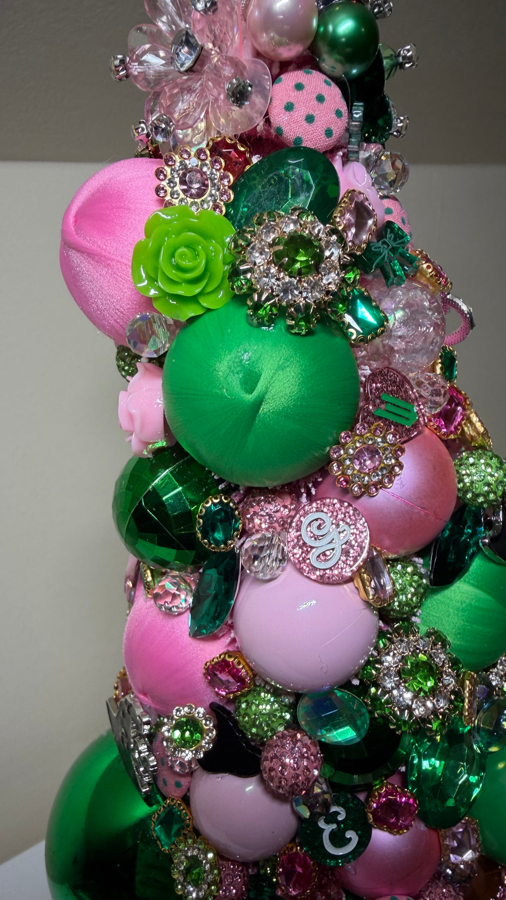 A colorful and decorative Christmas or Table Top tree made from pink and green ornaments, beads, and sequins, displayed on a white mantelpiece next to a round mirror.