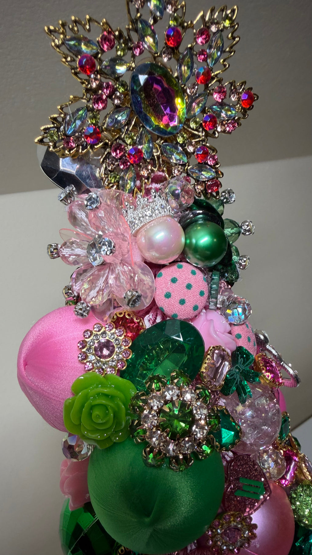 A one of a kind decorative Christmas or Table Top tree made from pink and green ornaments, beads, and sequins, displayed on a white mantelpiece next to a round mirror.