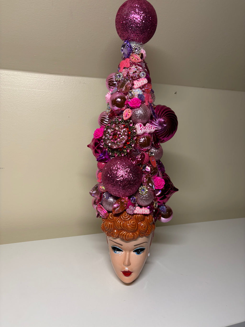 A decorative bejeweled doll themed Christmas or table top tree  made from pink and purple glittery ornaments, beads, sequins, and small embellishments, displayed in a vintage  Barbie 3D Mug