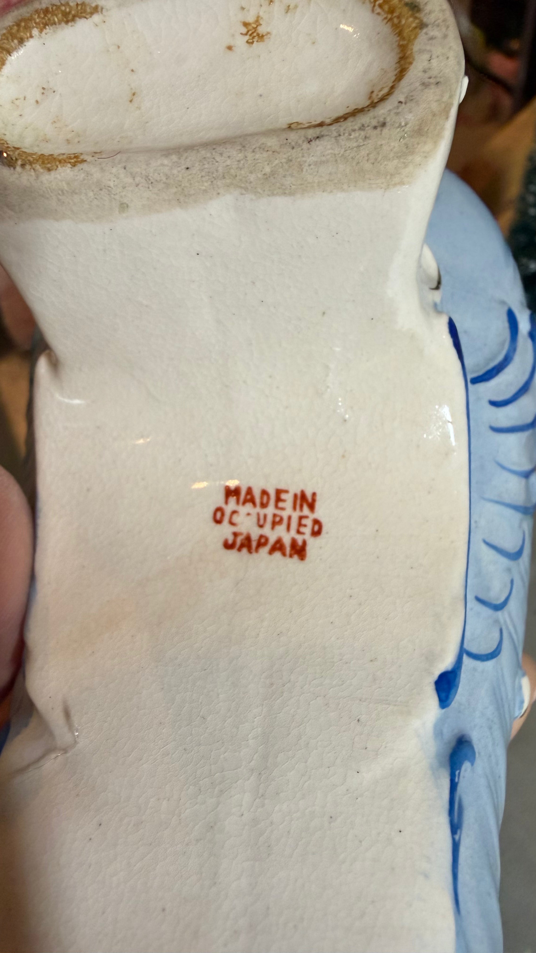 Close-up of the base of a white ceramic Japanese vessel, showing red text that reads 'MADEIN OCCUPIED JAPAN' and blue painted decoration along the side.