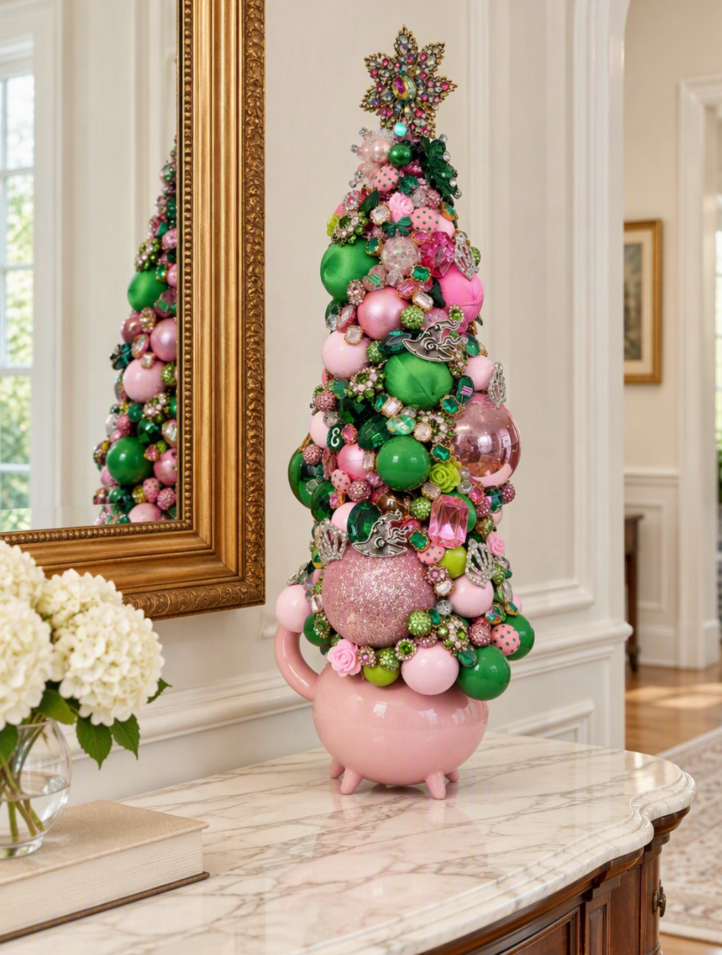 Beautiful highly embellished Christmas or table top tree covered in colorful rhinestones, pink and green ornaments, pearl-like beads, and glittery decorative elements against a plain indoor background.