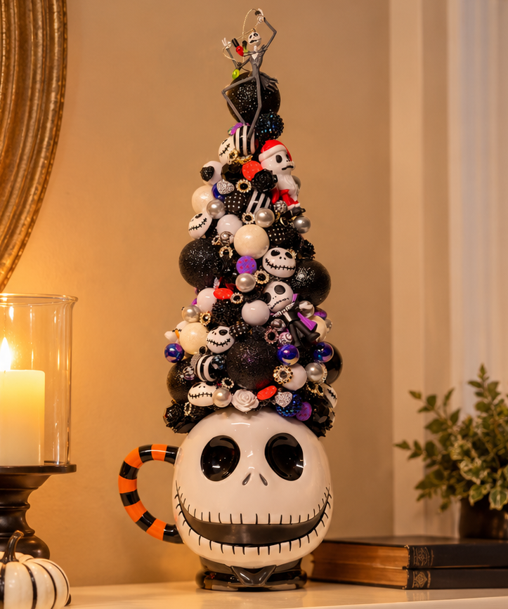 A decorative Jack Skellington mug shaped Christmas tree stands on a fireplace mantel in a warm holiday setting. The tree is made from a black mug with a white face and large black eyes, decorated with small black, white, and orange ornaments, beads, and a star topper.