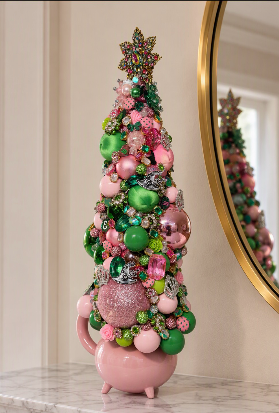 Elegant highly embellished Christmas or table top tree covered in colorful rhinestones, pink and green ornaments, pearl-like beads, and glittery decorative elements against a plain indoor background.
